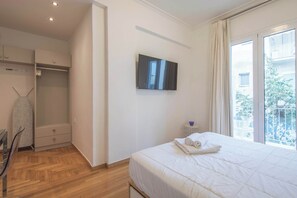 Une chambre à coucher comprenant un lit, une armoire, un miroir et une fenêtre donnant sur des immeubles.