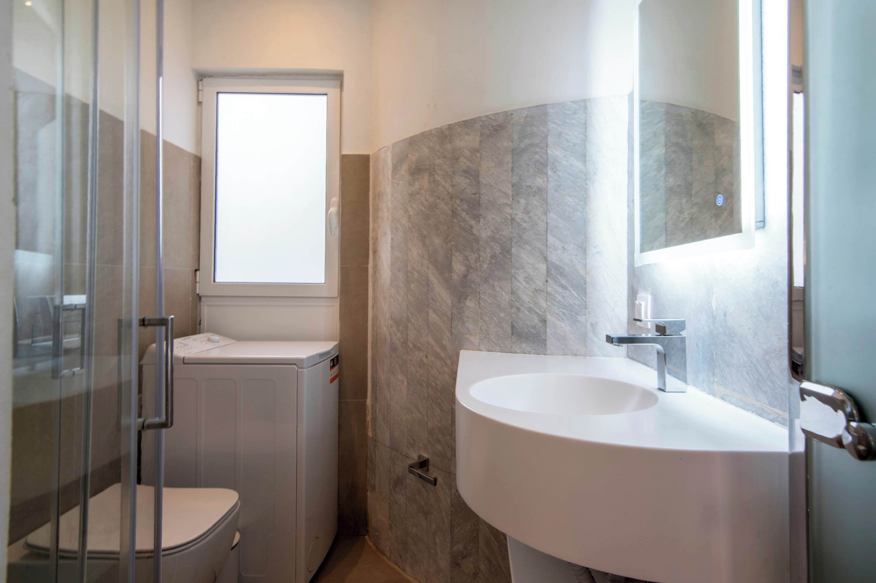 Une salle de bain avec une douche à parois de verre, des toilettes, un lavabo avec un miroir et une fenêtre.