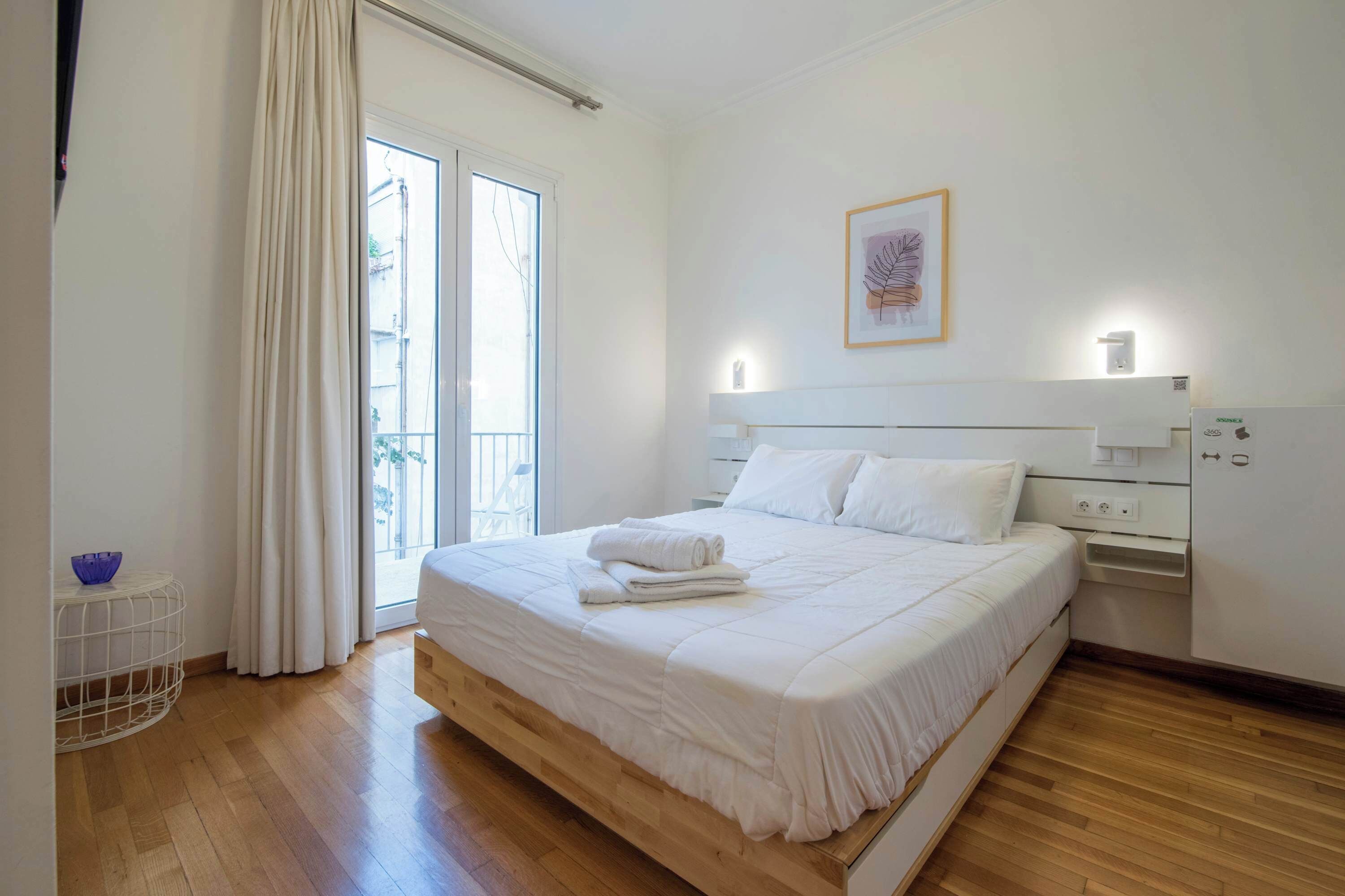 Un dormitorio con cama, mesita de noche, cortinas en la ventana y lámpara de pared.
