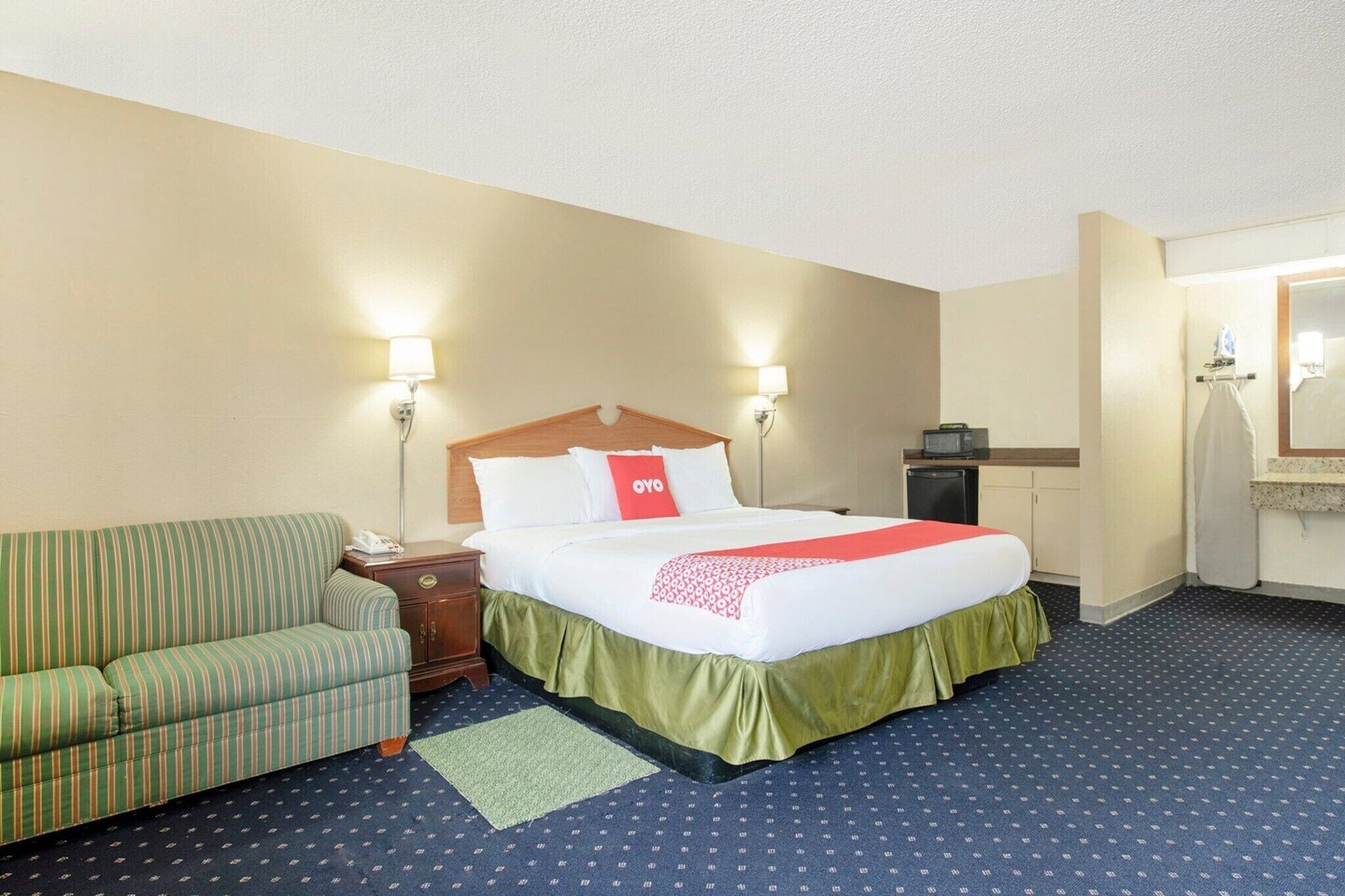 A hotel room with a bed, a green-striped sofa, a nightstand, a desk, and a mirror.