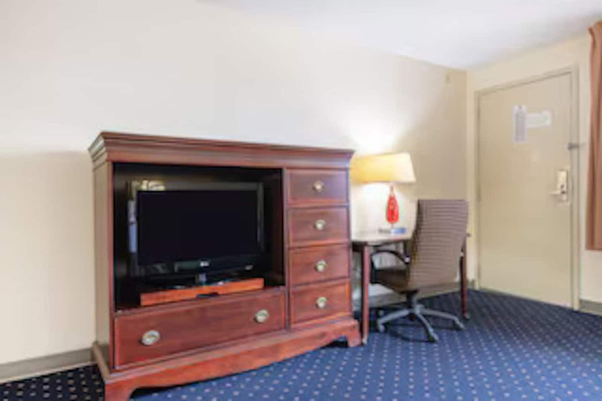 Een hotelkamer met een houten dressoir, een televisie, een bureau met een lamp en een stoel.