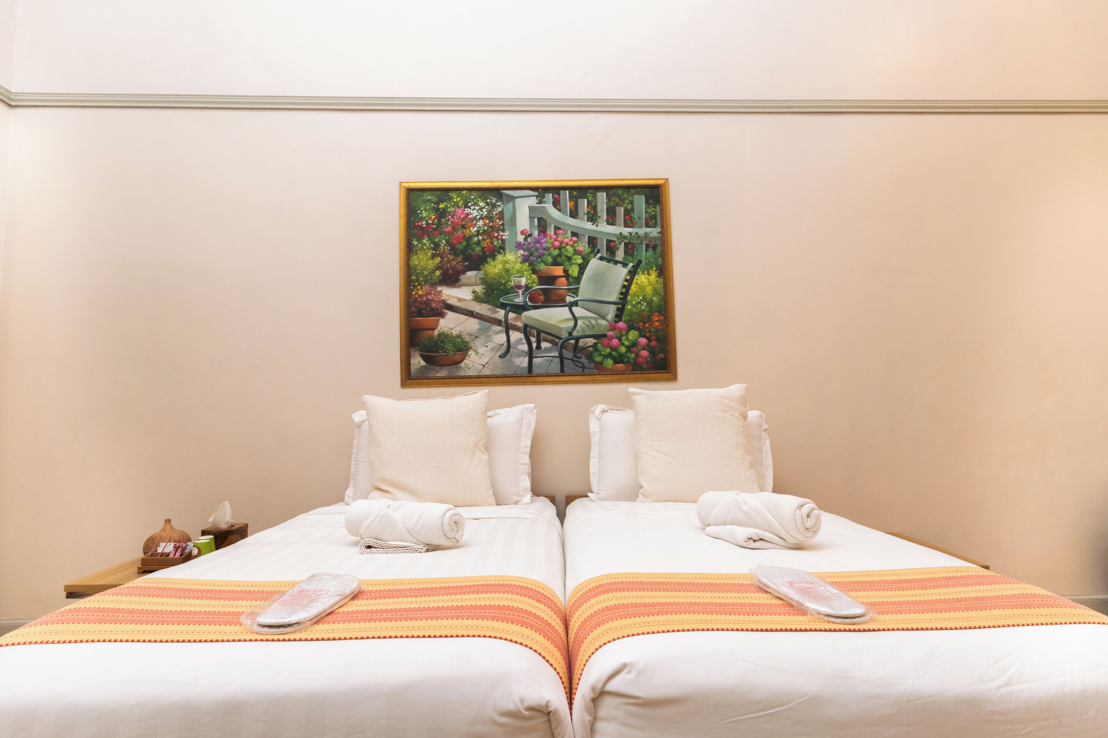 Ein Hotelzimmer mit zwei Betten, einem Gartenbild, einem kleinen Tisch und einem Sessel.