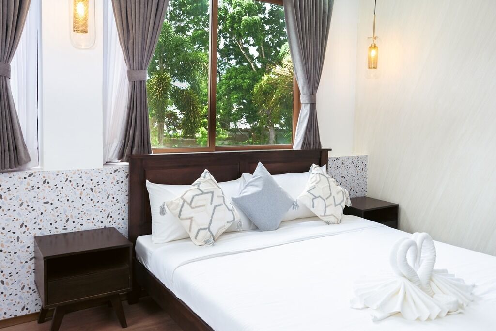 A hotel room with a bed, nightstands, a window with curtains, and a view of trees.
