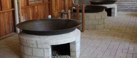 Un espace de cuisine traditionnel avec un grand wok posé sur un poêle en pierre, un mur en briques et un sol carrelé.