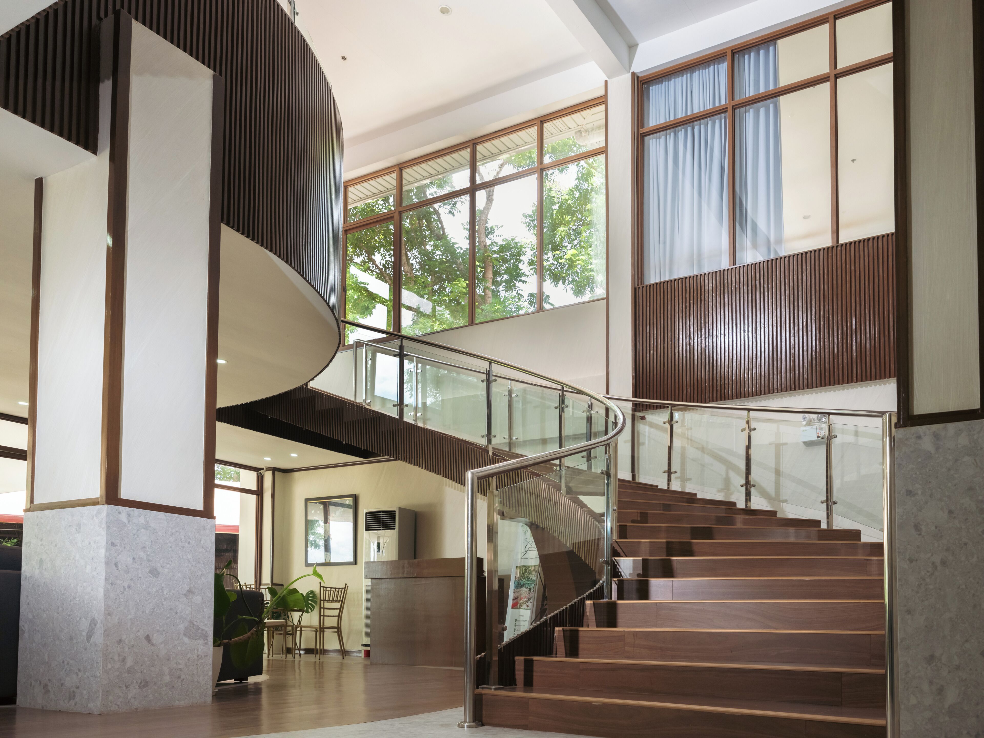 Ein modernes Interieur mit einer geschwungenen Treppe, großen Fenstern und einem Essbereich.