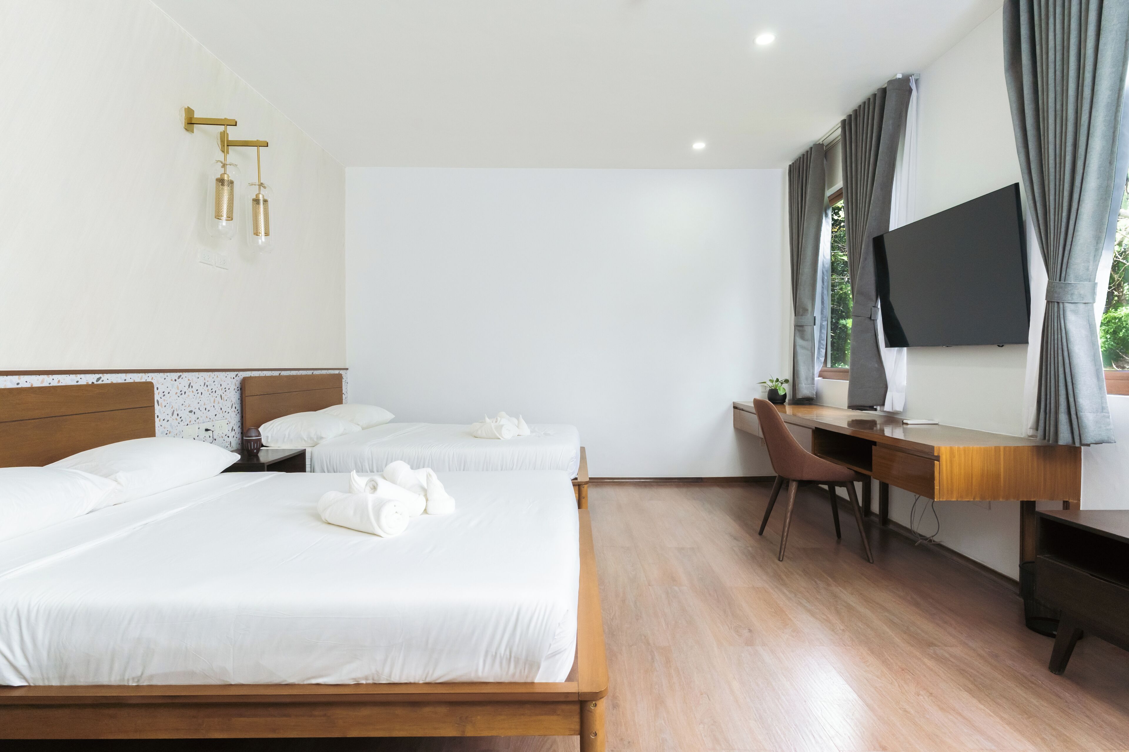 A hotel room with two beds, a desk, a chair, a television, and a wall-mounted light fixture.