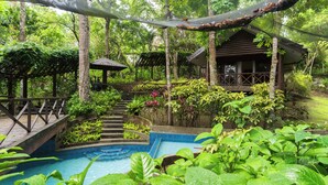 A pool surrounded by lush greenery, wooden steps leading up to a gazebo, and a small building with a sloped roof. - The Glens Tagaytay (Tagaytay)