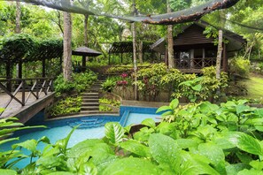 A pool surrounded by lush greenery, wooden steps leading up to a gazebo, and a small building with a sloped roof. - The Glens Tagaytay (Tagaytay)