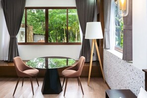 A room with a round table, two chairs, a floor lamp, and a window with a view of greenery. - The Glens Tagaytay (Tagaytay City)