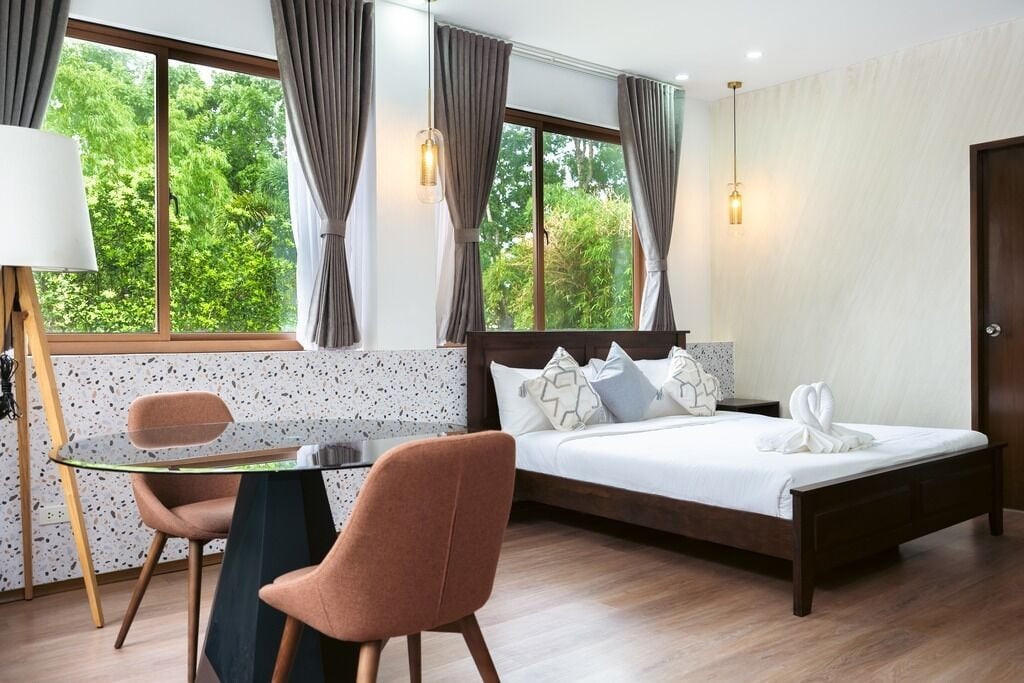 Un dormitorio con cama, una mesa, dos sillas, una lámpara y cortinas.