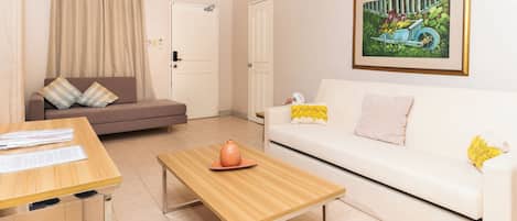 A living room with a sofa, a coffee table, a dining table, and a painting on the wall.