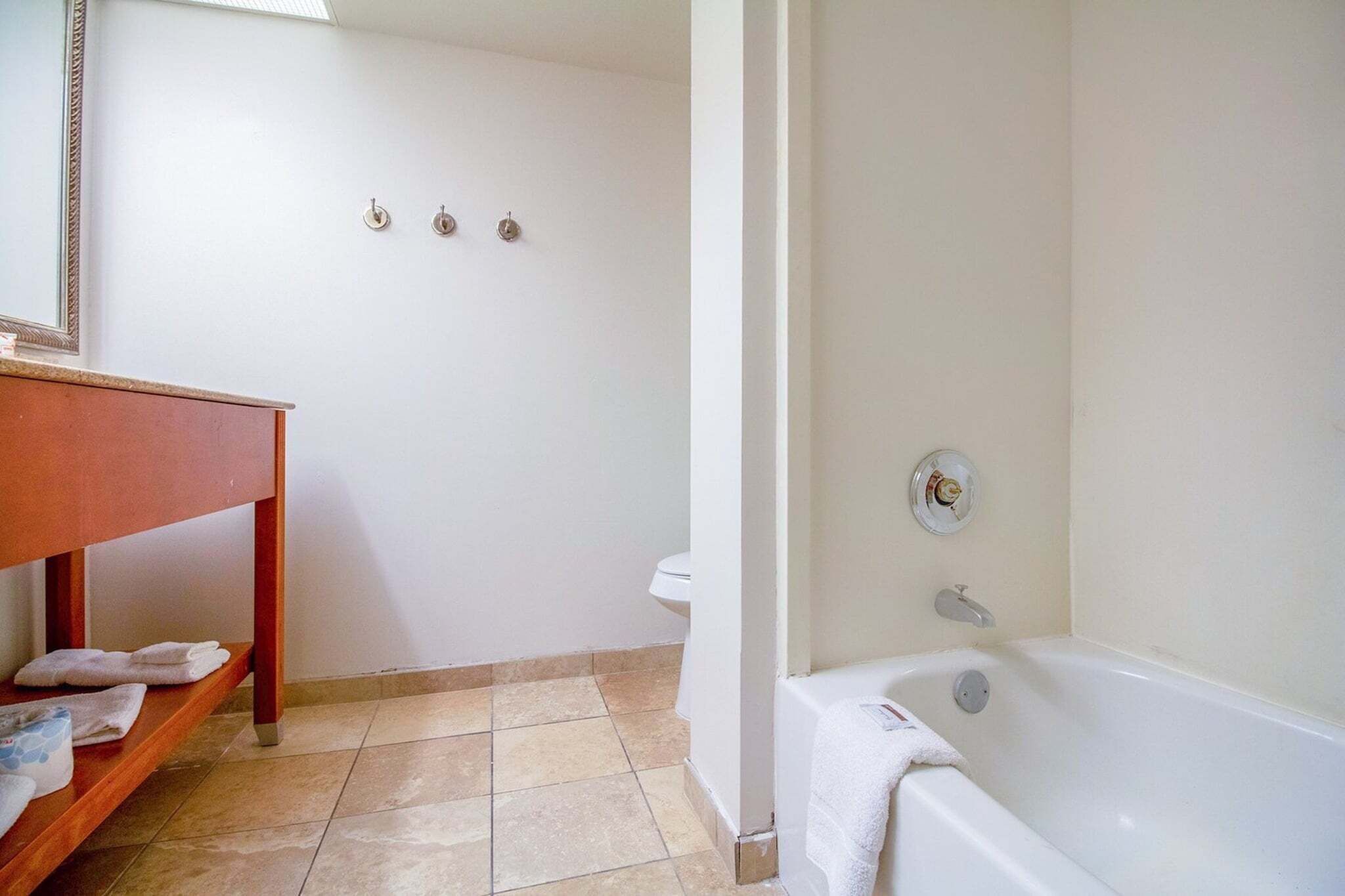 A bathroom with a bathtub, a toilet, a sink with a mirror, and a shelf with towels.
