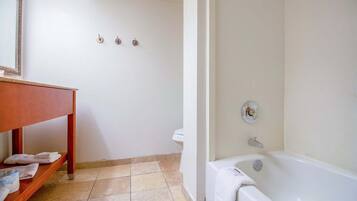 A bathroom with a bathtub, a toilet, a sink with a mirror, and a shelf with towels.