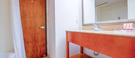 Une salle de bain avec une porte en bois, un rideau de douche blanc, un miroir au-dessus d’un lavabo et un porte-serviettes.