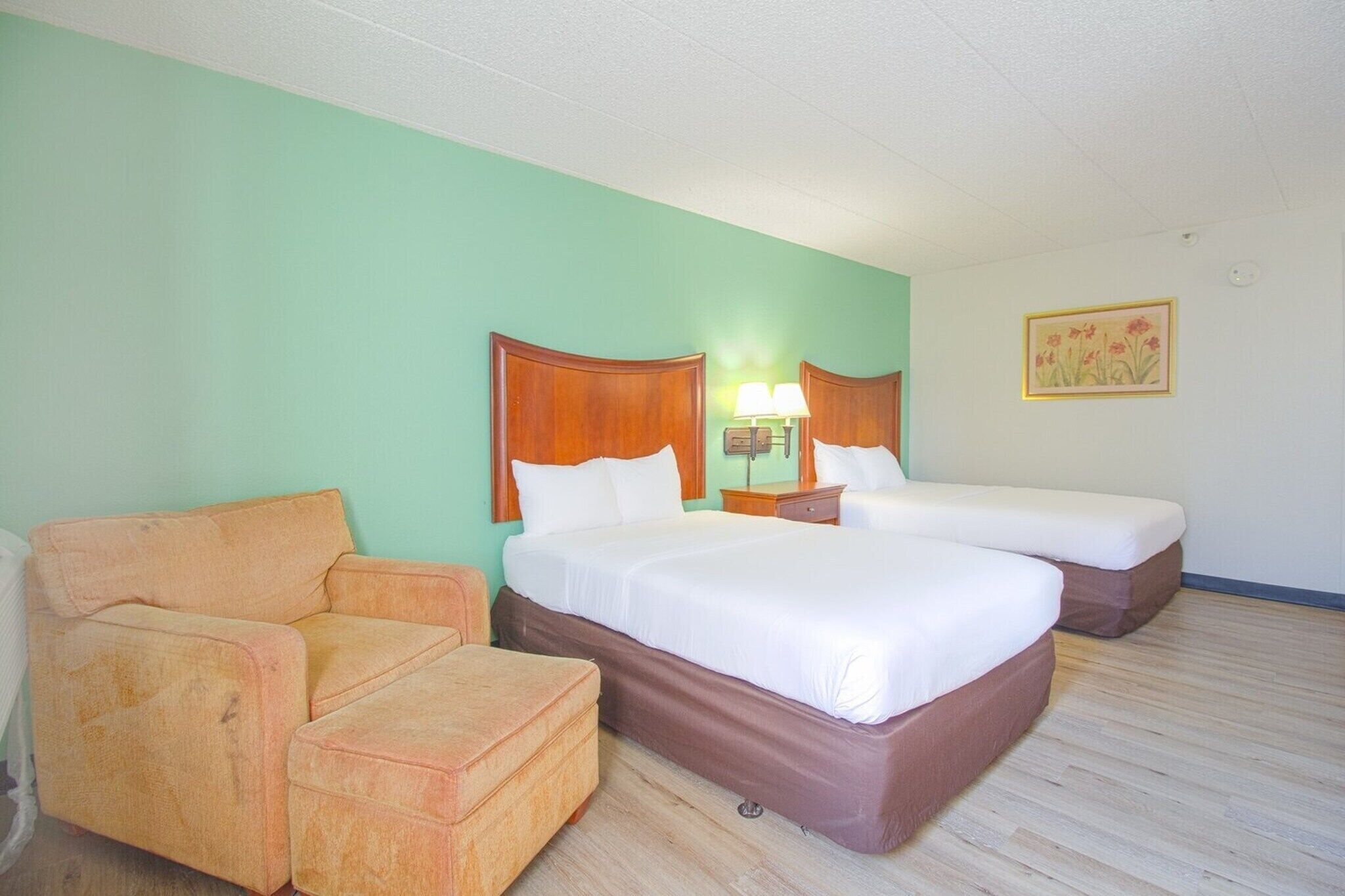 A hotel room with two beds, a chair, a nightstand with lamps, and a painting on the wall.