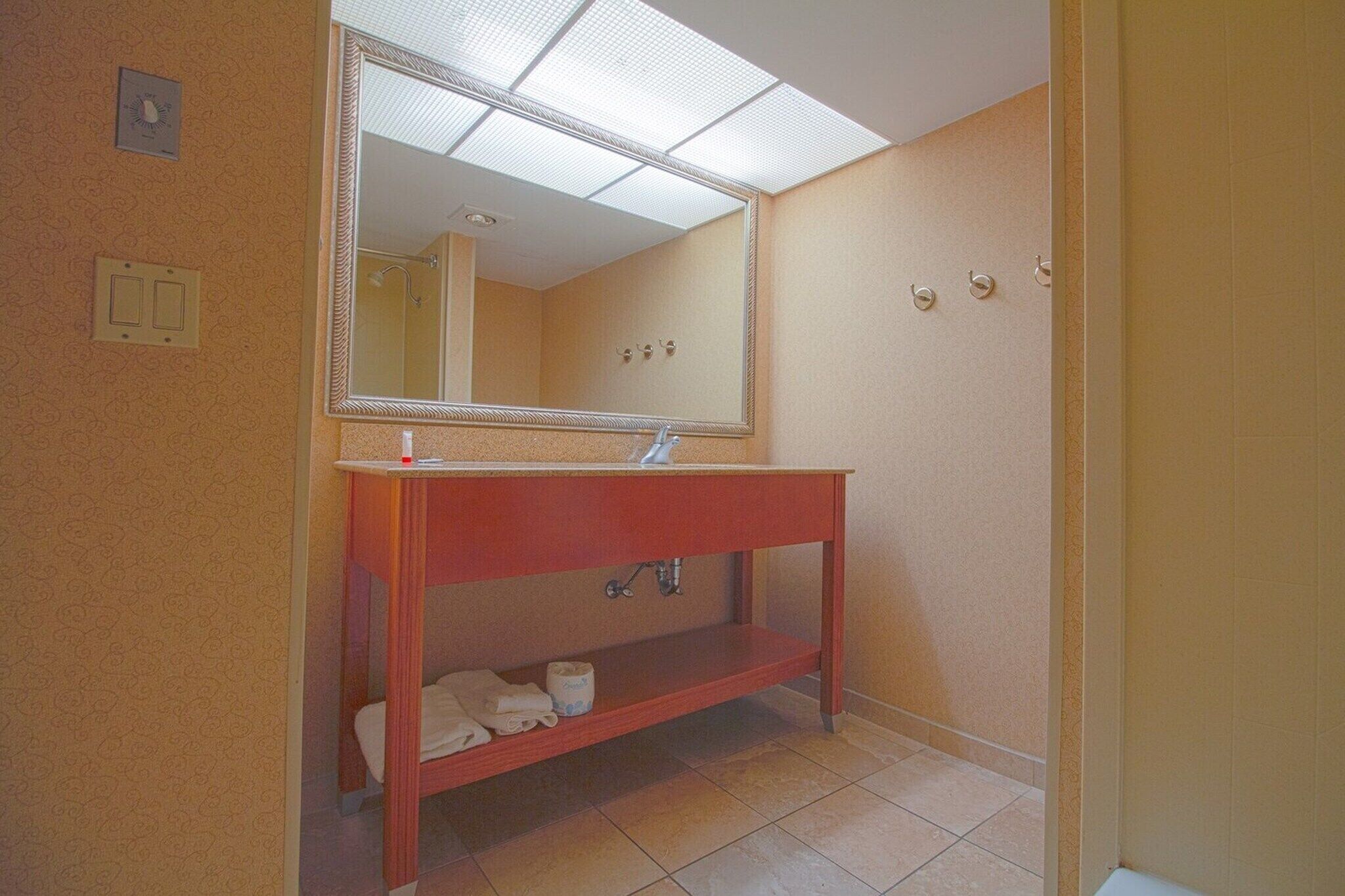 A bathroom with a wooden vanity, a mirror, a toilet, and a shower area.