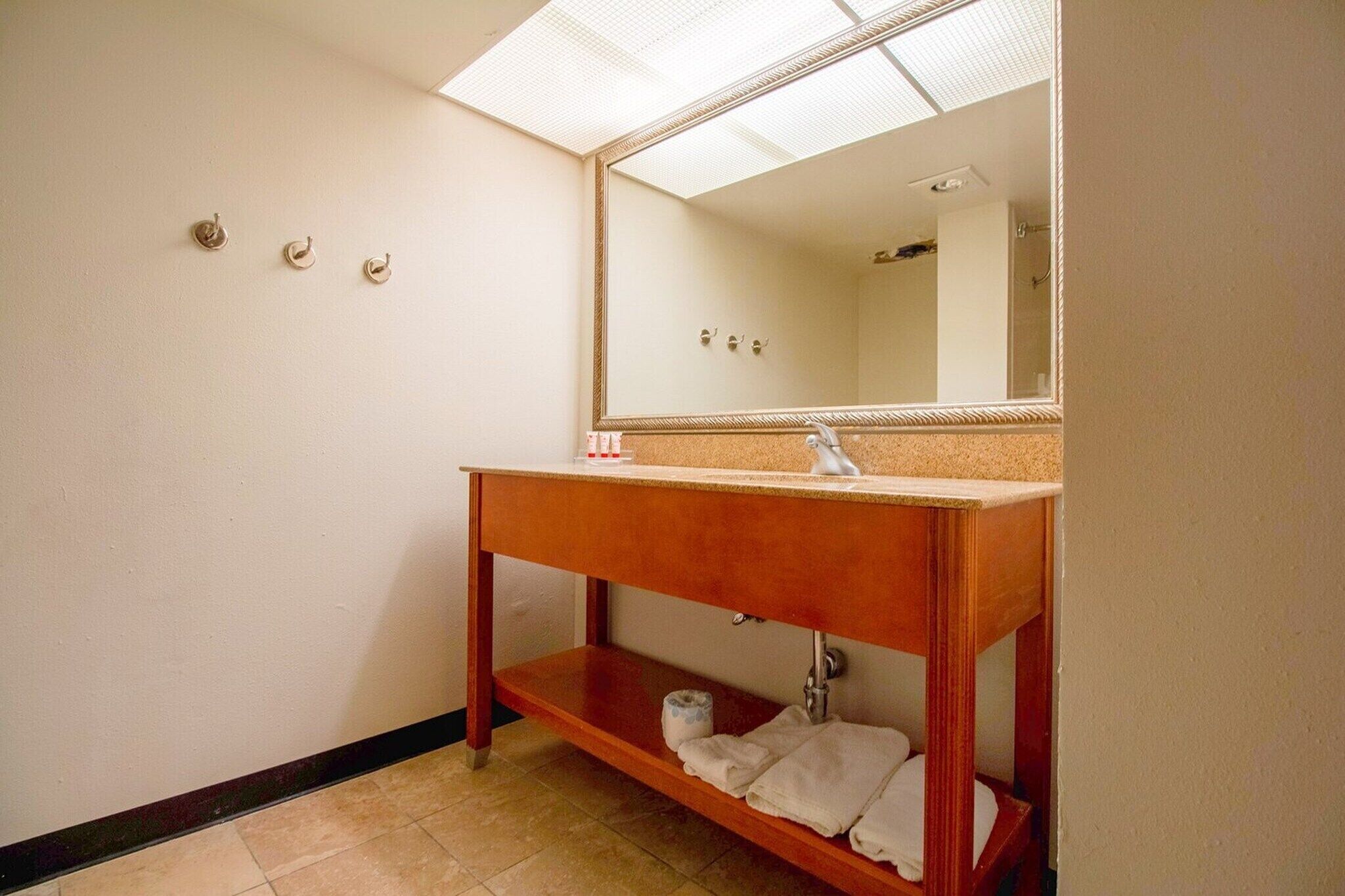 Une salle de bain avec un meuble-lavabo en bois, un miroir, un évier et une étagère avec des serviettes.