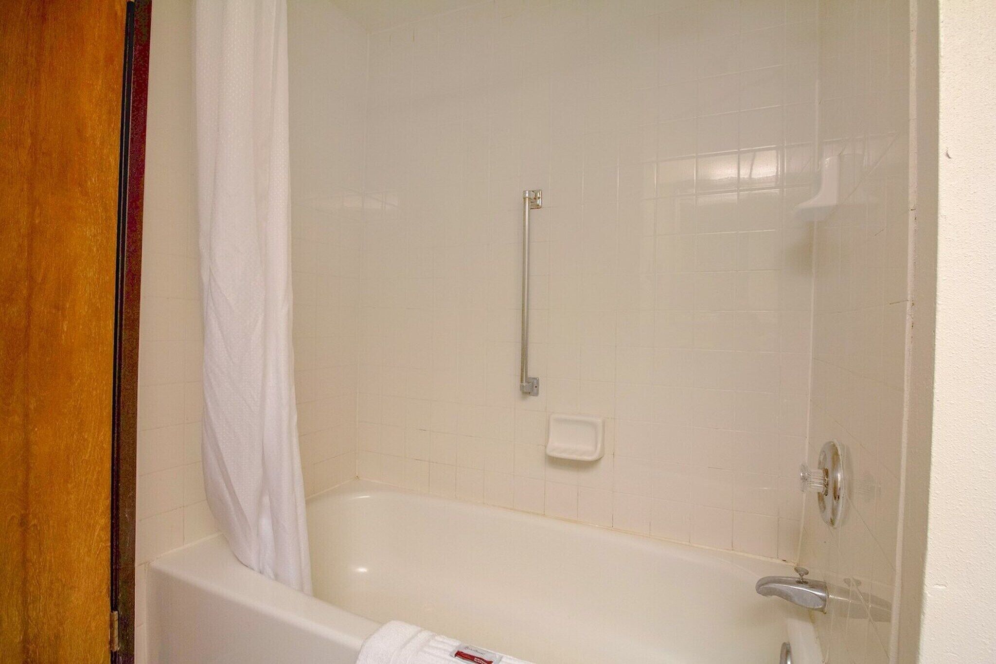 A bathroom with a bathtub, a shower curtain, a towel rack, and a soap dish.