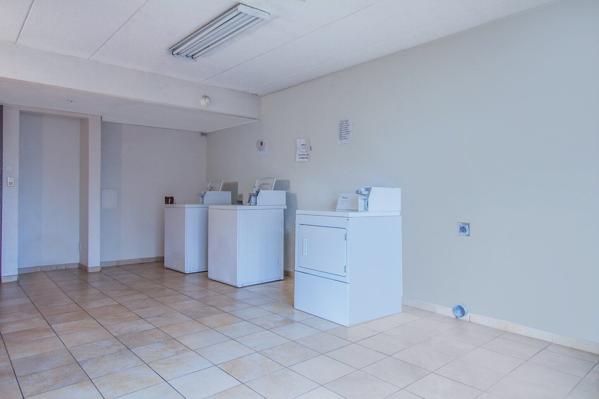A laundry room with three white washers and dryers, a tiled floor, and a door leading to another room.