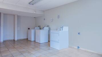 A laundry room with three white washers and dryers, a tiled floor, and a door leading to another room.