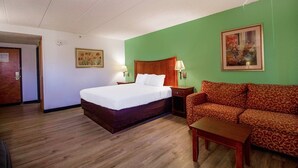 Hotellihuone, jossa on sänky, sohva, pieni pöytä ja taulu seinällä.