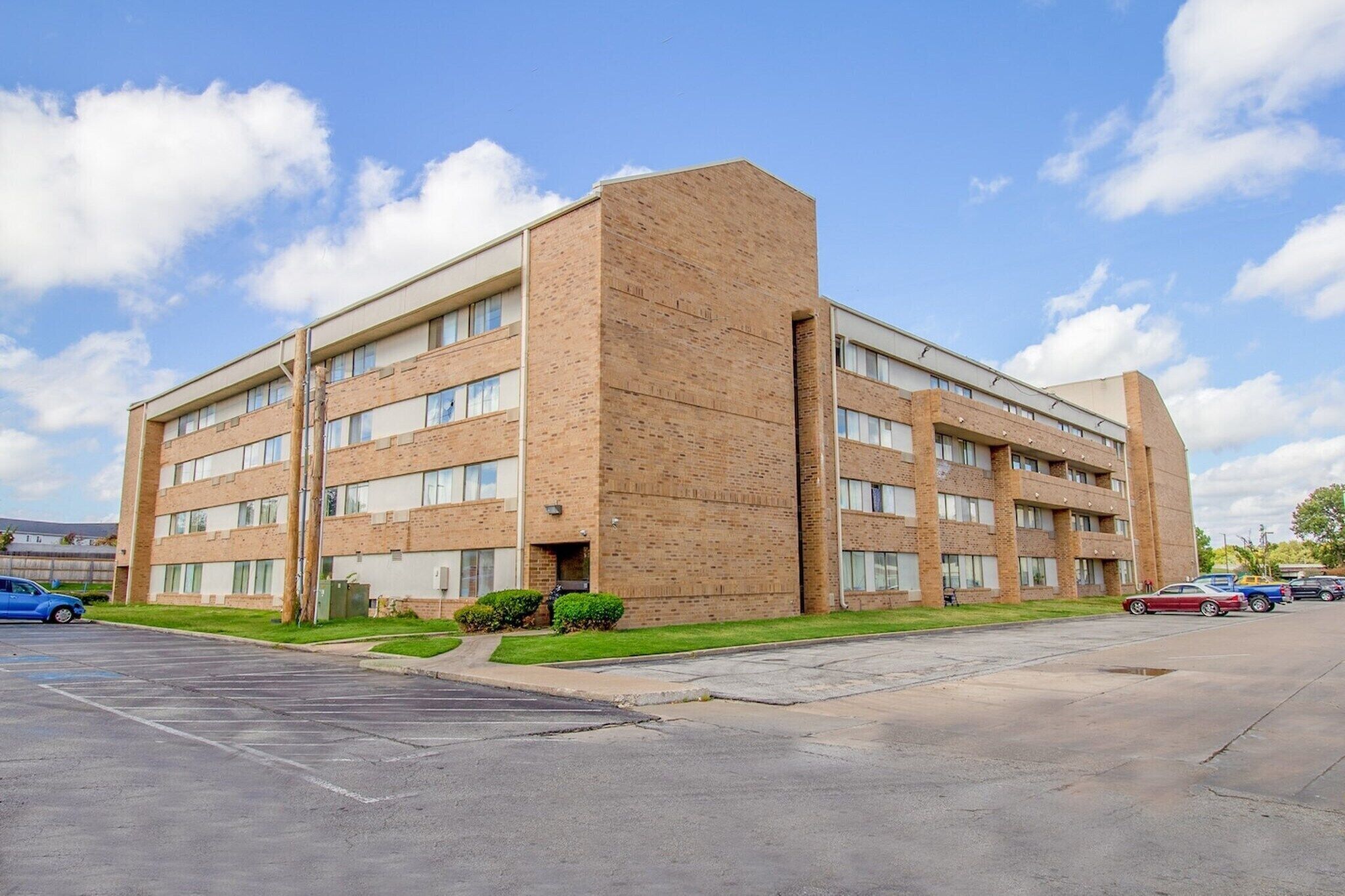 A multi-story building with a brick facade, parking lot, and green landscaping.