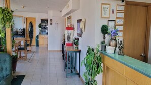 A hotel lobby with a reception desk, a dining area, and a kitchen in the background.