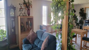 A living room with a sofa, a wooden cabinet, a clock, and various plants.