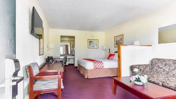 A hotel room with a bed, a sofa, a desk, a chair, a TV, and a mirror.