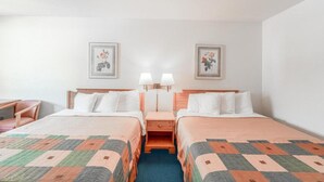 A hotel room with two beds, a desk, two nightstands with lamps, and two framed pictures on the wall.