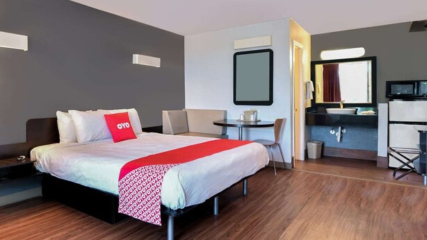 A hotel room with a bed, a desk, a chair, a mirror, a TV, and a bathroom. - King Bed|Non Smoking (Valdosta GA)