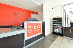 A reception desk with a red wall, a sign reading 'OYO HOTEL,' and a shelf with cleaning supplies. - Premium King Bed|Nsmk (Valdosta GA)