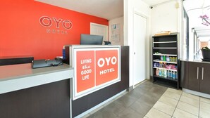Un comptoir d’accueil avec un mur rouge, une enseigne indiquant « OYO HOTEL », et une étagère contenant des produits de nettoyage.