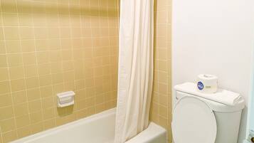 Un bagno con pareti piastrellate di giallo, una vasca da bagno bianca, un water bianco con porta carta igienica e un telo da doccia bianco.