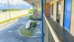A covered outdoor area with a parking lot, a building with blue doors, and a large white object on the grass. - 2 Full Beds Non-Smoking (Valdosta GA)
