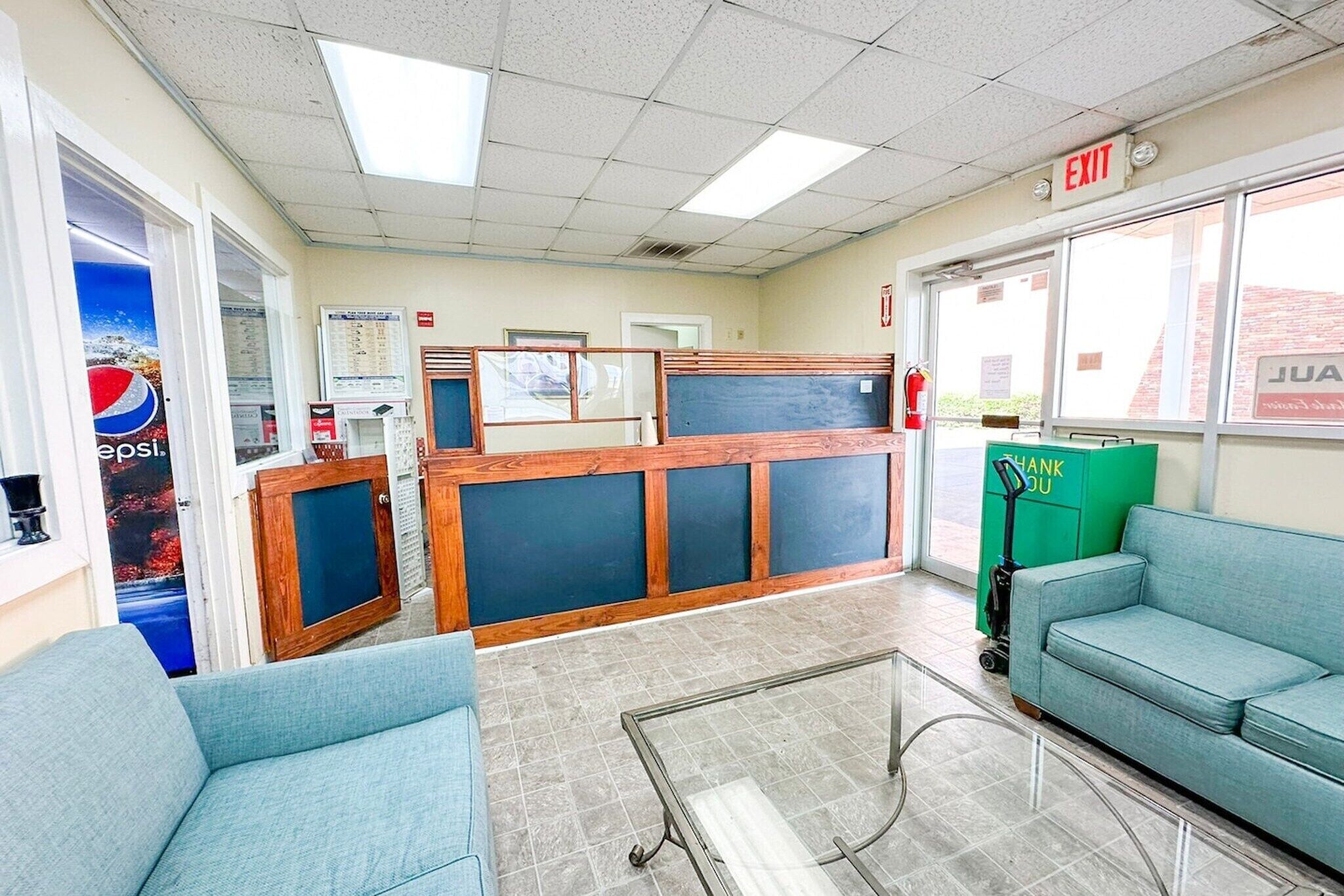 A lobby with a reception desk, blue seating, a glass coffee table, and a Pepsi advertisement.