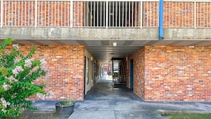 A brick building with a covered walkway, a potted plant, and a metal railing. - 2 Full Beds Non-Smoking (Valdosta GA)