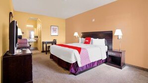 A hotel room with a bed, bedside tables, a desk, a television, and a bathroom visible through an archway.
