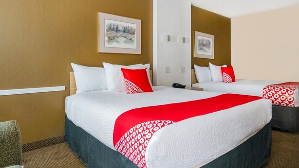 A hotel room with two beds, white bedding, red accents, and framed artwork on the walls. - 2 Queen Bed| Non smoking (Wichita Falls TX)