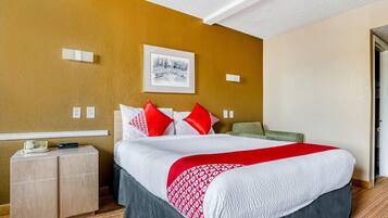 Hotelkamer met een bed, nachtkastje, nachtlampje, een ingelijst schilderij aan de muur en een deur aan de rechterkant.