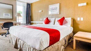 Habitación de hotel con una cama grande, un escritorio, una silla, un banco y una ventana con cortinas.