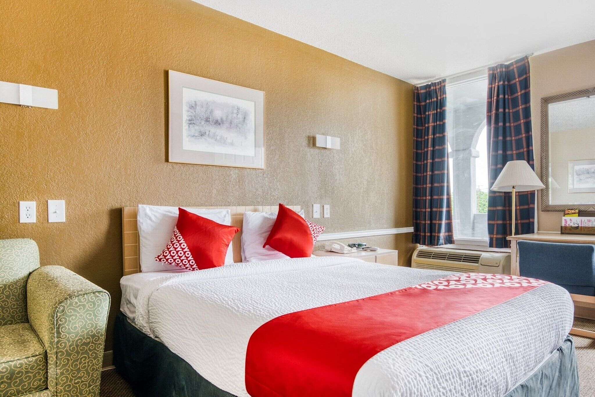 A hotel room with a bed, a chair, a desk, a lamp, and a window with curtains.