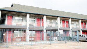 A multi-story building with a row of rooms, each with a red door and barred windows.