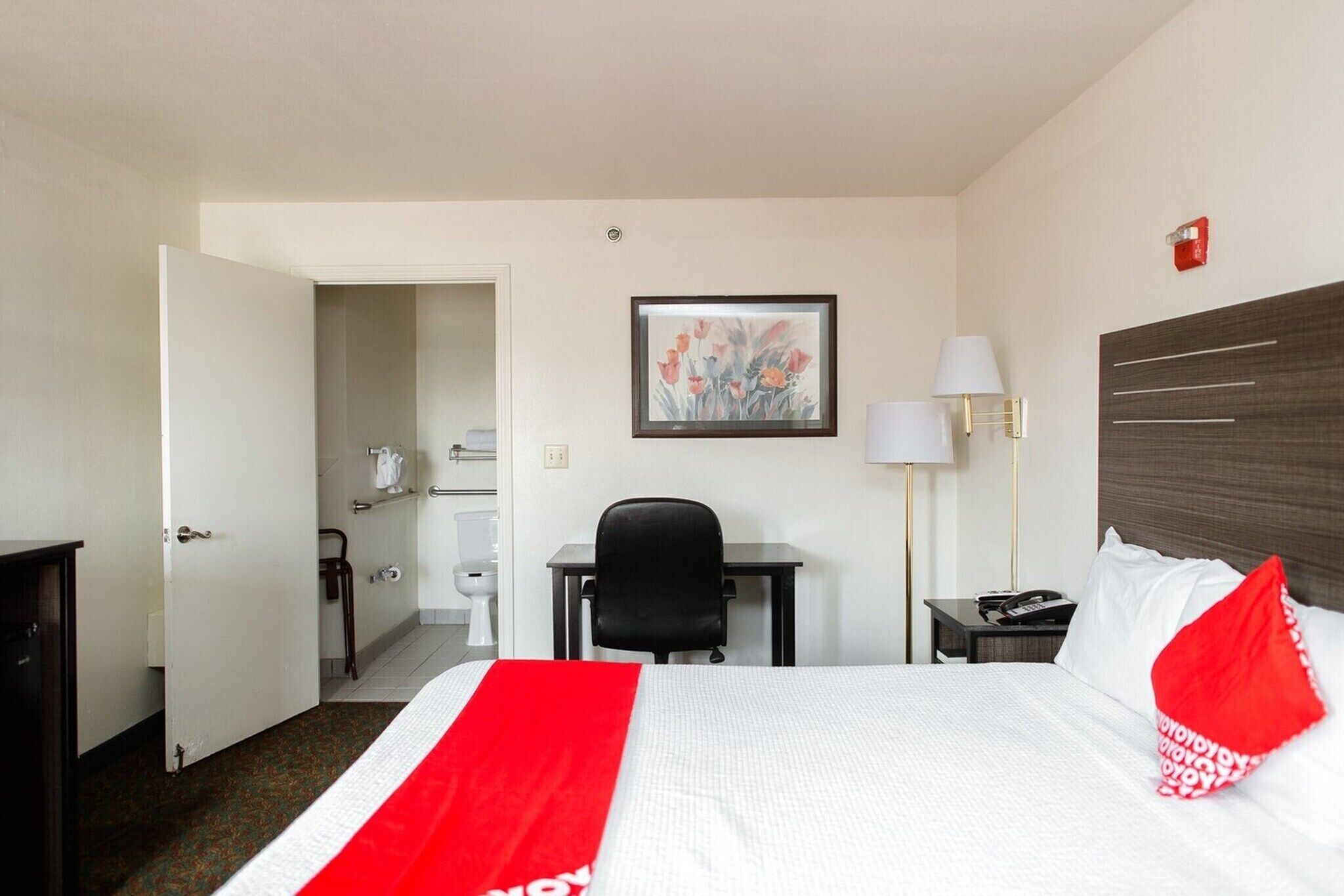 A hotel room with a bed, desk, chair, and a painting on the wall.