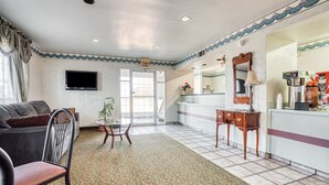 A hotel lobby with a sofa, a small table, a mirror, a coffee machine, and a TV on the wall.