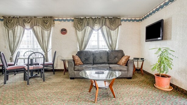 A living room with a sofa, chairs, a glass coffee table, a potted plant, and a television.