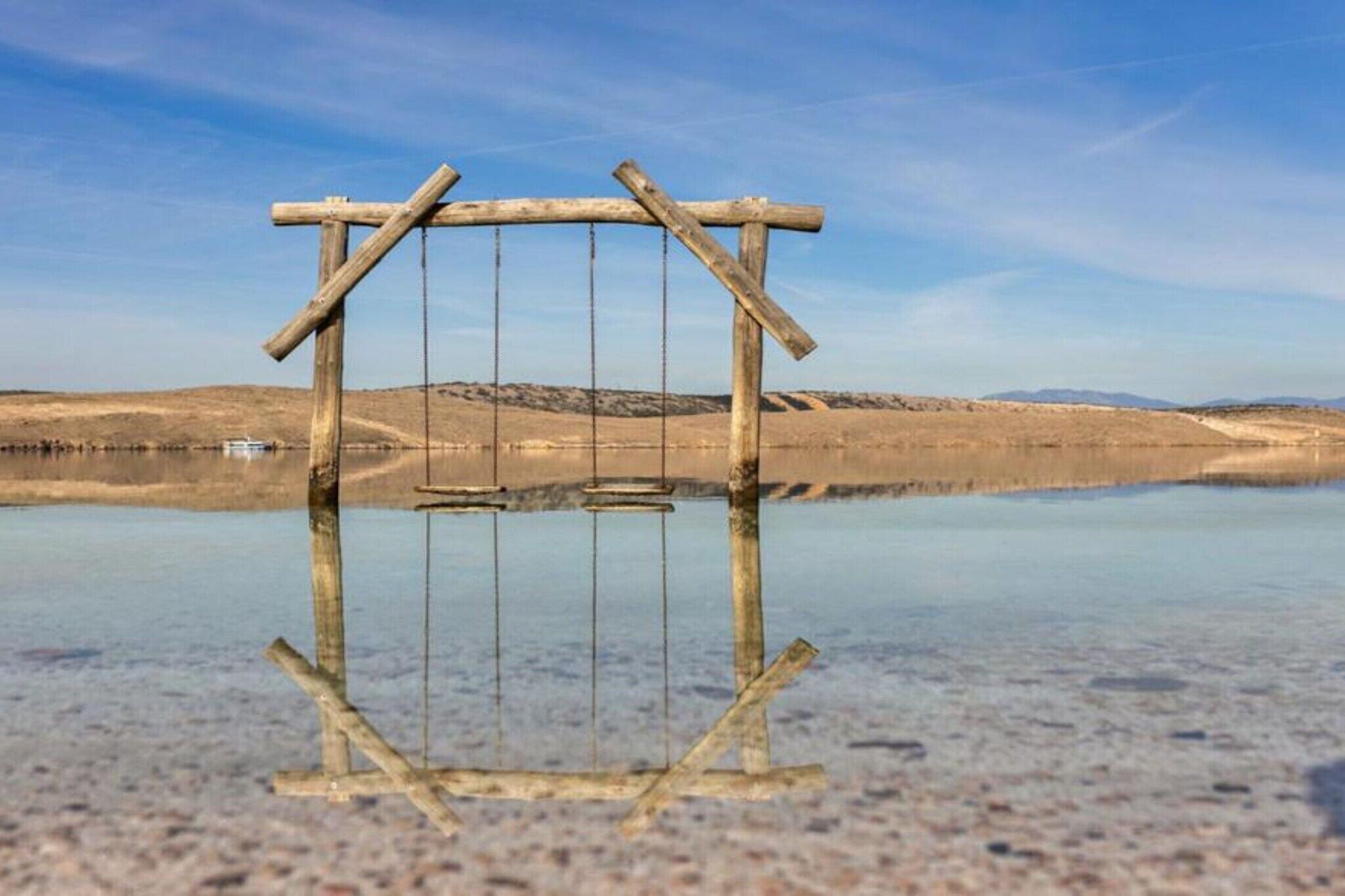 Eine Holzhütte in einer weiten, offenen Landschaft mit einem Gewässer, das den Himmel und die fernen Hügel spiegelt.