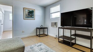 Een woonkamer met een televisie, een lijst met een afbeelding aan de muur, een klein tafeltje en een bank.