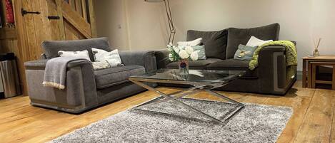 A living room with a grey sofa, a glass coffee table, a grey shag rug, wooden flooring, a staircase, and framed pictures on the wall.