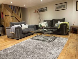 A living room with a grey sofa, a glass coffee table, a grey shag rug, wooden flooring, a staircase, and framed pictures on the wall.